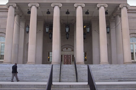 Person walks up the front steps of a large building towards the entrance.